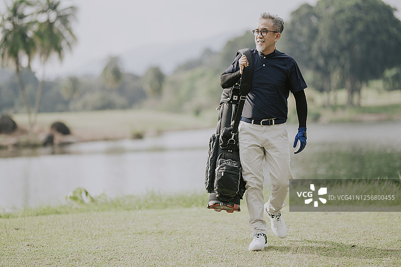 一个成熟的中国男子高尔夫球手背着一个高尔夫球袋在高尔夫球场看向别处图片素材