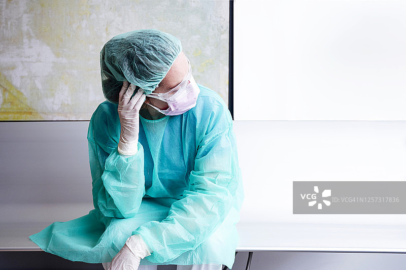悲伤的医生穿着防护服靠墙坐在医院里图片素材
