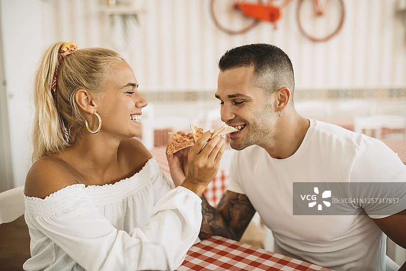 一个快乐的年轻女人坐在餐馆里给男朋友吃披萨图片素材