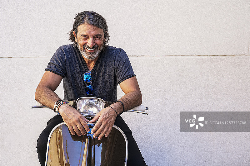 快乐成熟的男人坐在摩托车上靠白墙图片素材