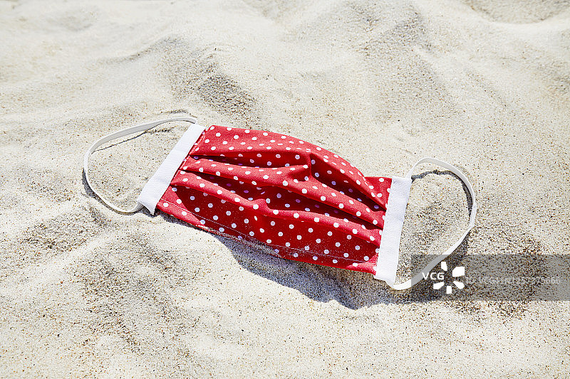 高角度的观点，一个红色的自制面膜在海滩上，度假与一个保护性的面膜图片素材
