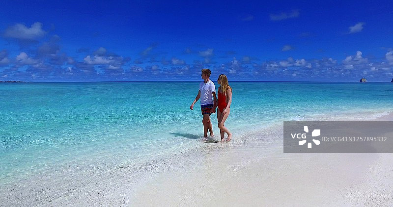 年轻幸福的夫妇走在海滩上，手牵手微笑着环视彼此。图片素材