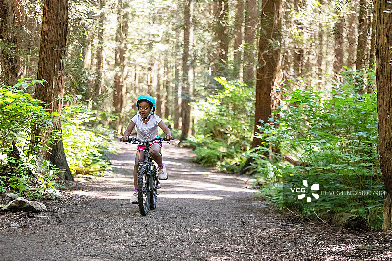 年轻女孩在森林小径上骑自行车图片素材
