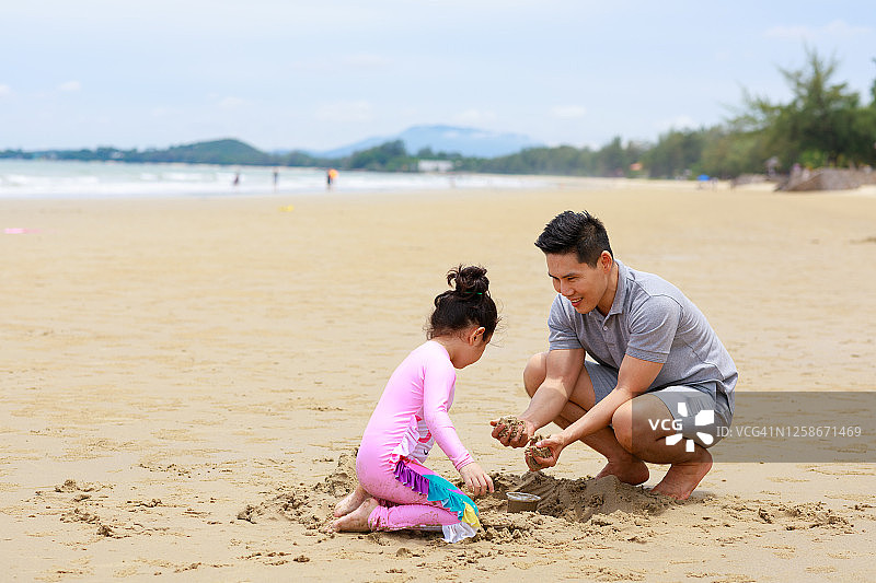 单身父亲假期和女儿在沙滩上玩沙子。图片素材