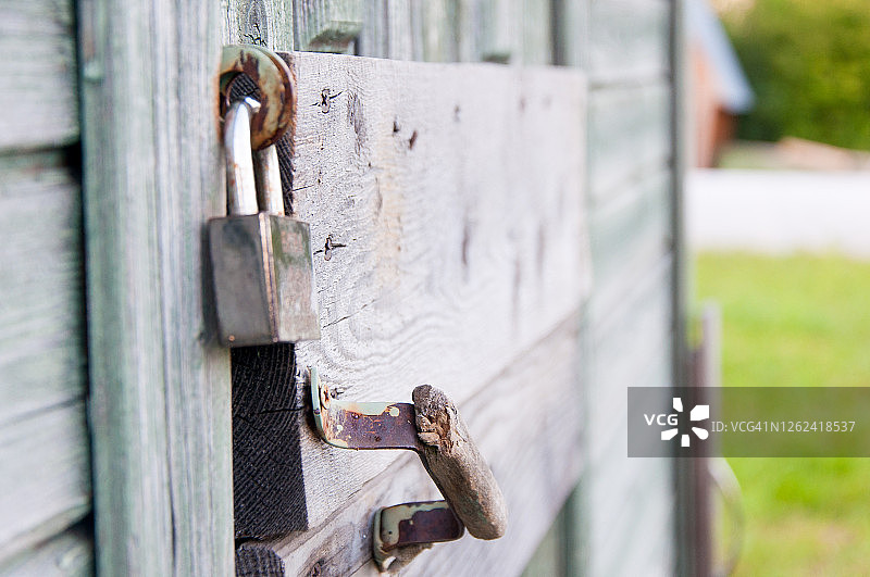 这把旧锁是用来锁旧木门的。钢制银锁可靠地锁住旧门，门上油漆剥落。城堡特写。挂锁的详细视图。旧木门上的生锈的锁。图片素材