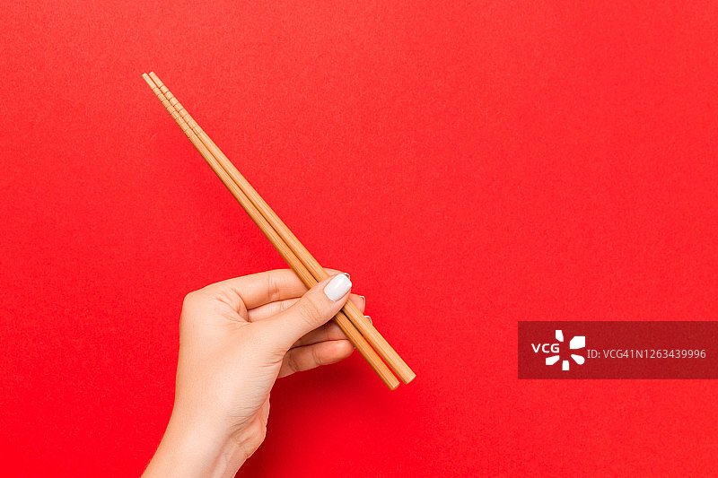 裁剪图像的女性手拿筷子在红色的背景。日本美食概念与复制空间图片素材
