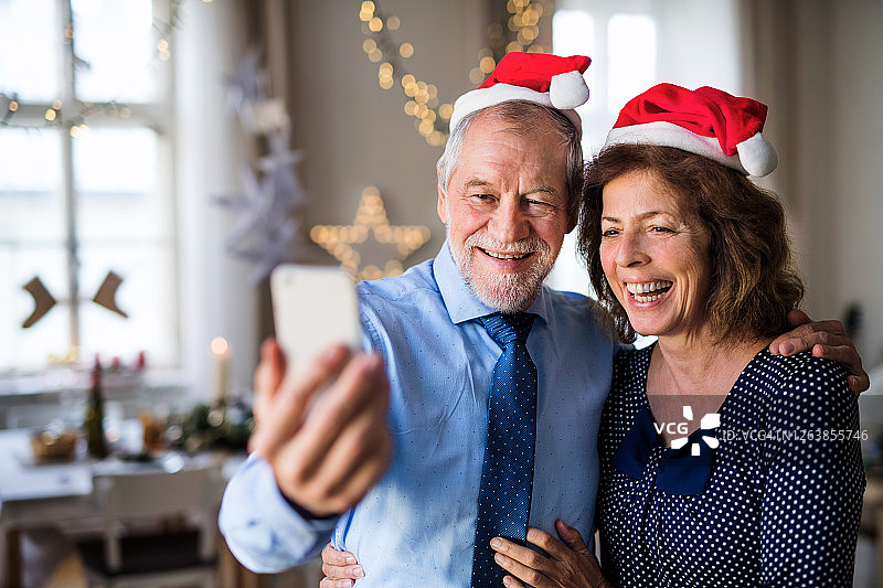 圣诞期间，一对老夫妇在室内用智能手机自拍。图片素材