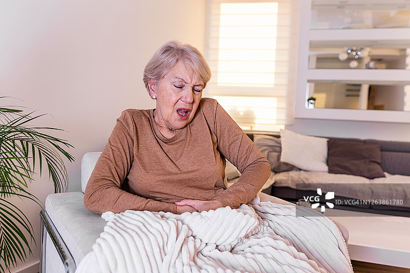 老年人的健康问题和人们的观念——老年妇女在家遭受胃痛。在家里忍受胃痛的资深女性图片素材