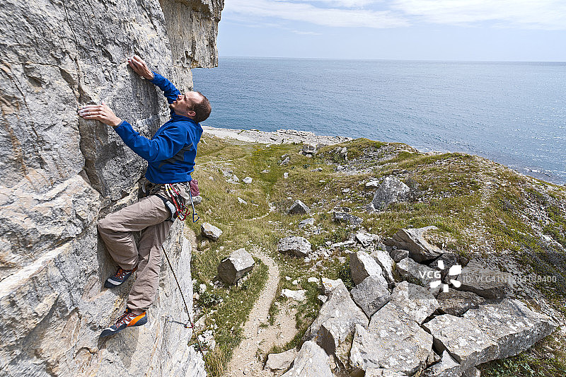 一名男子在英国斯瓦尼奇海岸附近的石灰岩悬崖上攀爬图片素材