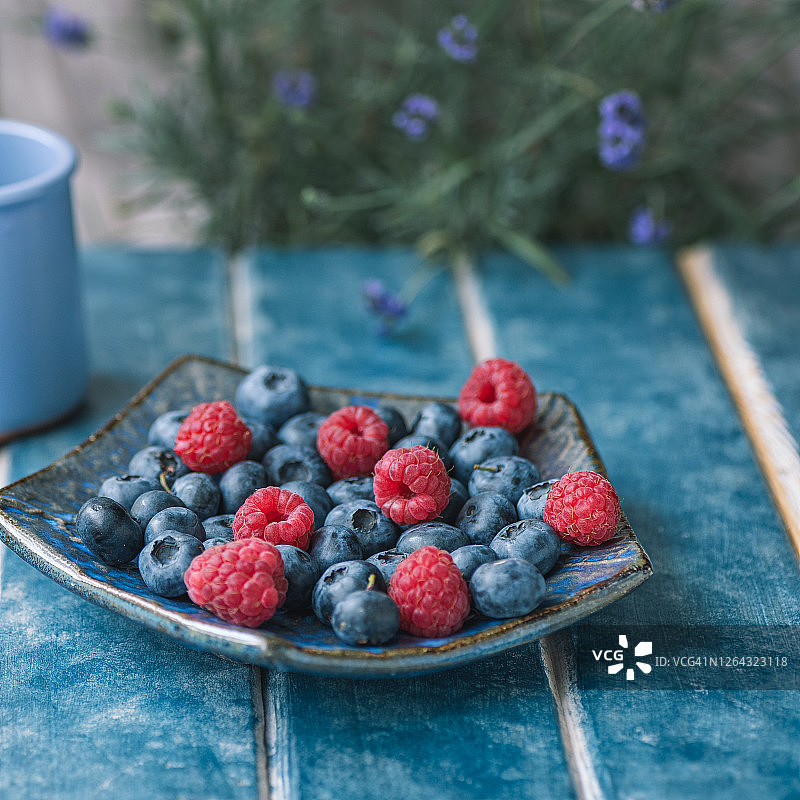 食品的背景。民族盘蓝莓，覆盆子。蓝色背景上的薰衣草。图片素材
