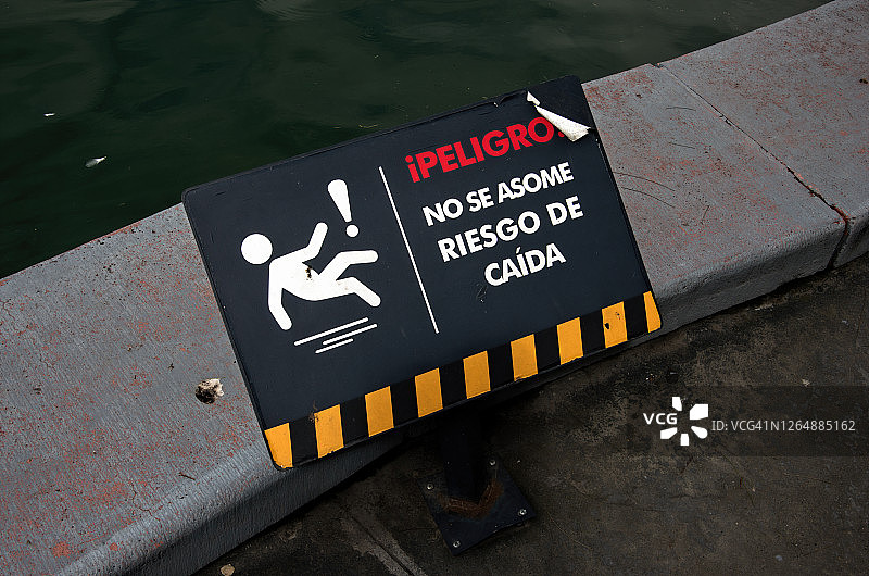池塘边的窗台上立着一个西班牙语标牌，上面写着“佩里格罗!”没有一些riesgo de caída'[危险!不要冒坠落的风险]图片素材