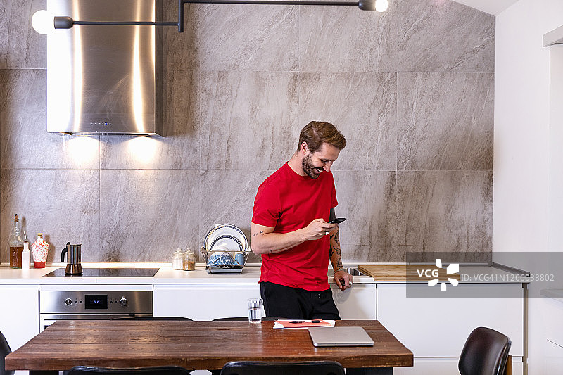 微笑的中年男人站在厨房柜台边用智能手机图片素材