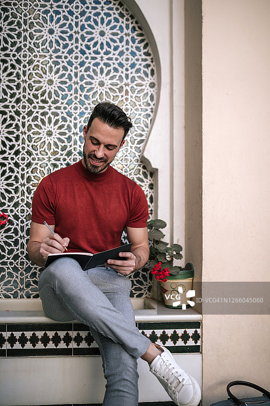 微笑的男人坐在窗台上写书图片素材
