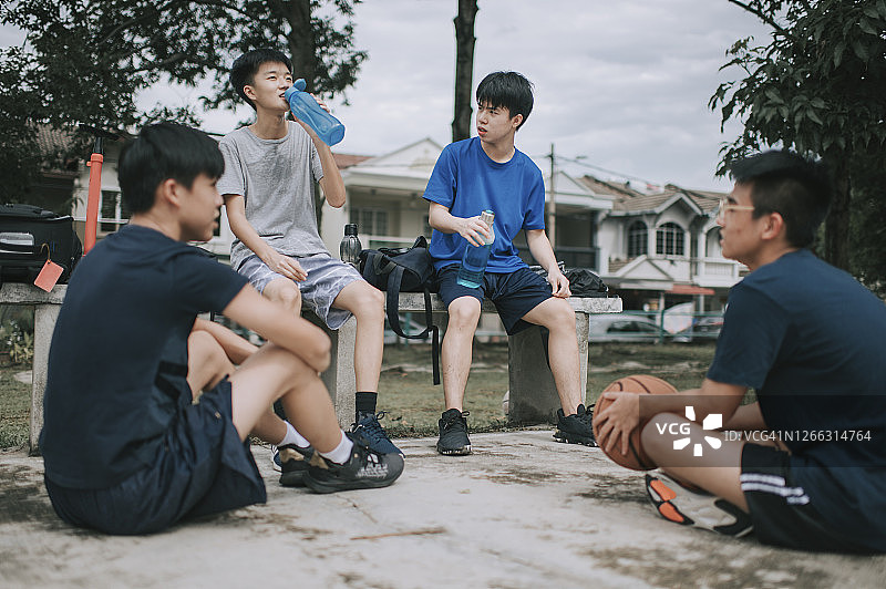 一群十几岁的亚洲华人男孩在放学后在篮球场上打篮球和练习篮球后休息和休息图片素材