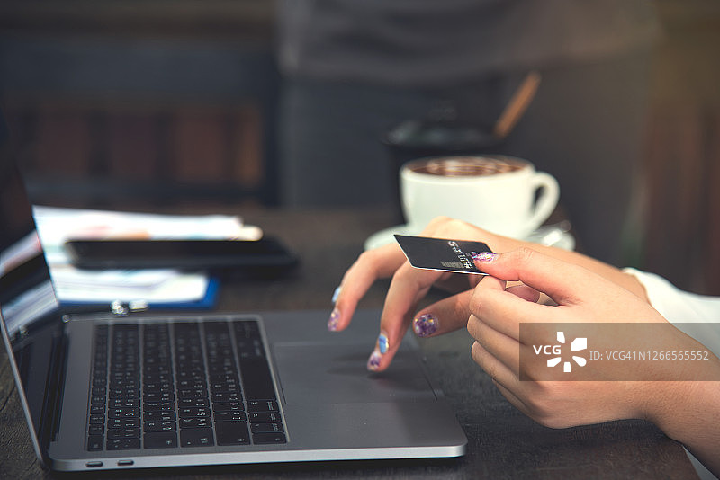 购物和支付通过信用卡在线社交网络的概念。年轻女性使用信用卡在电脑上支付账单，在互联网上的技术。图片素材