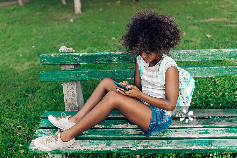 放学后坐在长凳上玩智能手机的女学生图片素材