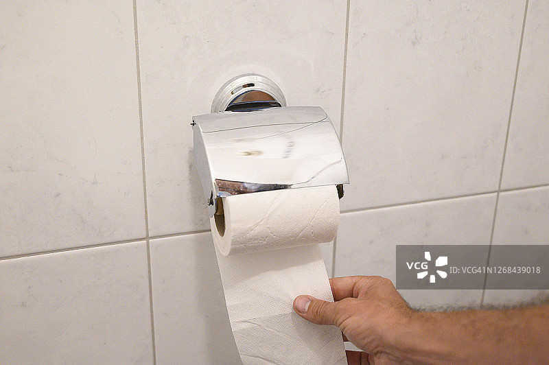 Man´s hand picking up a piece of toilet paper from a bathroom. Germany.图片素材
