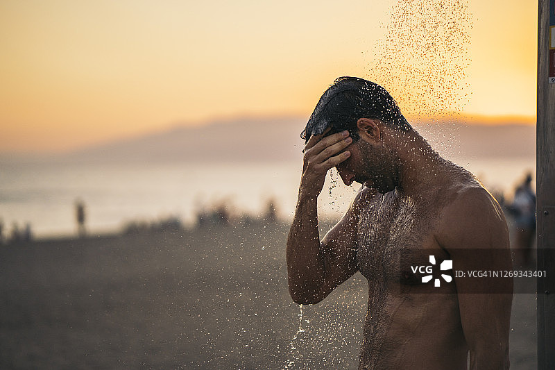 赤膊男子在日落时在海滩上冲凉图片素材