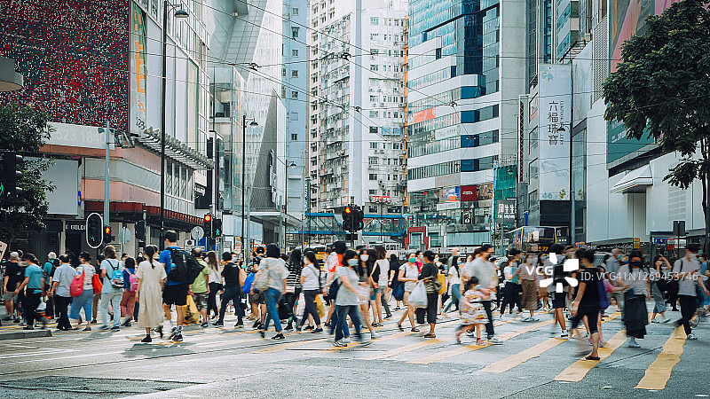 典型的香港城市生活。在繁忙的交通高峰时段，一群忙碌的上班族穿过市中心的街道，与现代的摩天大楼和城市交通形成对比图片素材