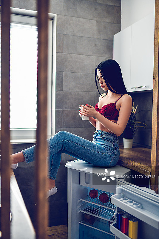坐在厨房柜台上喝咖啡的女性图片素材