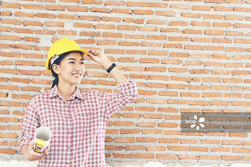 年轻美丽的工程师手持建筑图纸，戴着黄色头盔。图片素材