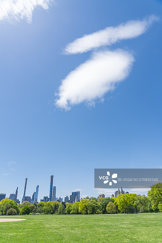 大云朵飘过中央公园的大草坪和曼哈顿中城的摩天大楼。图片素材