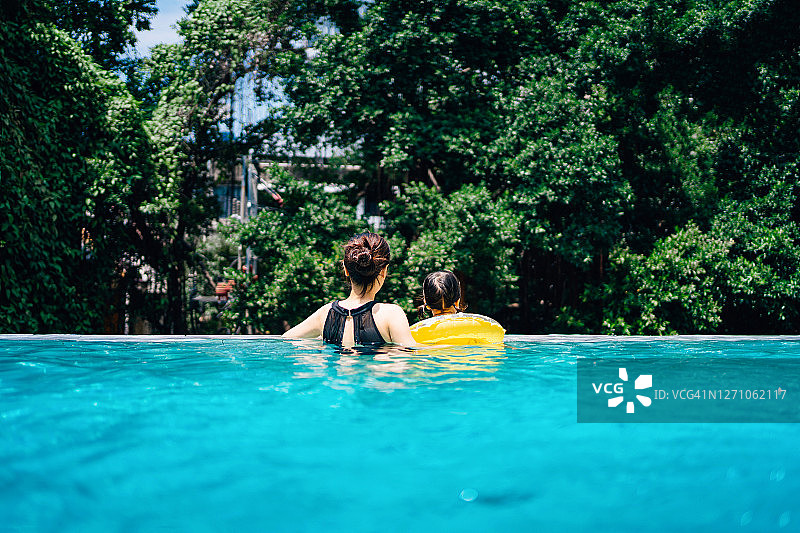 后视图的年轻的亚洲母亲和她的小女儿享受家庭团聚时间放松和在游泳池在夏天有乐趣图片素材