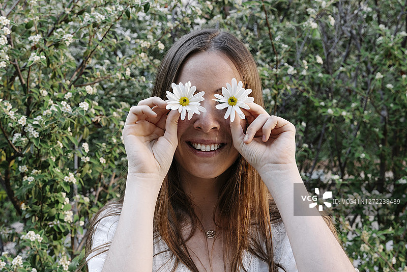 在春天的公园里，微笑的女人用白色的花遮住眼睛图片素材