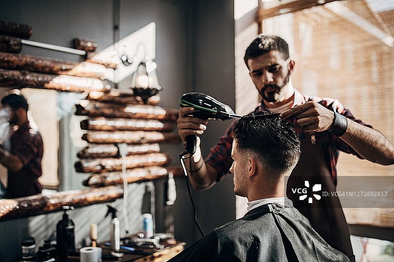 男理发师在理发店里吹干男人的头发图片素材