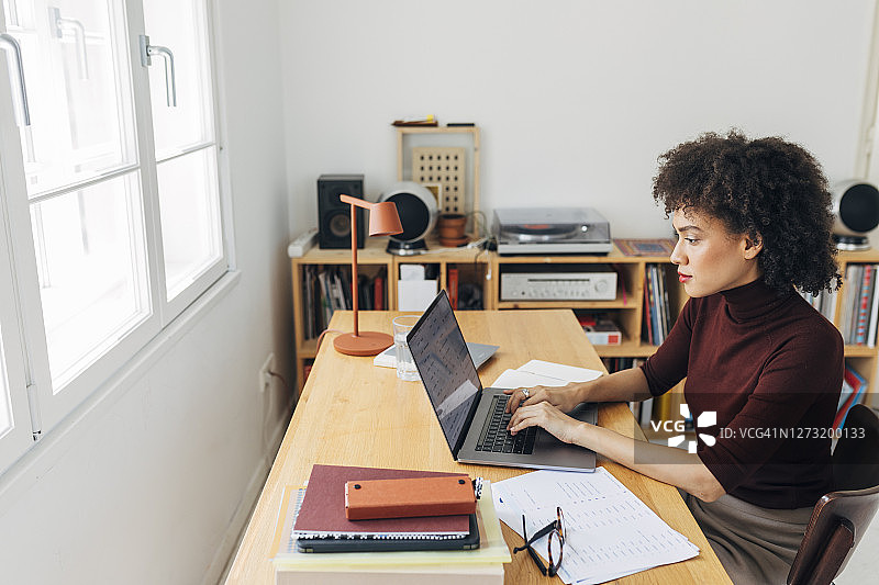 在家庭办公室:非洲裔美国妇女坐在她的办公桌和工作在她的笔记本电脑图片素材