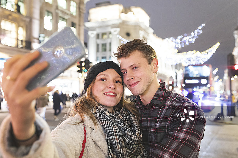 晚上在城市的圣诞彩灯下，女人和男朋友自拍图片素材