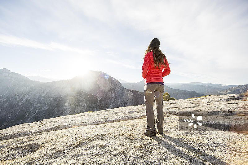 一个女人站在一座多岩石的山上，远处有半圆丘。图片素材