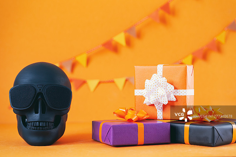 万圣节彩色礼盒与骷髅在橙色的背景。节日，生日，万圣节派对庆祝概念。图片素材