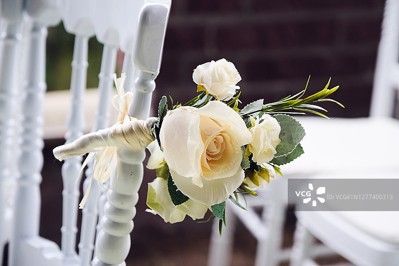 白色的木椅上装饰着鲜花和鲜艳的缎带，是婚礼仪式上的装饰。图片素材