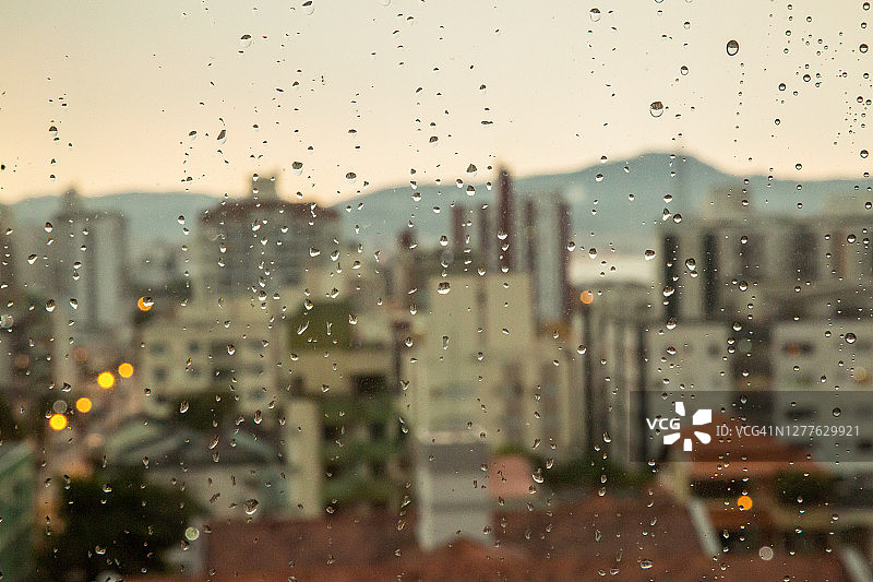 雨点打在窗玻璃上，使背景中的建筑物模糊不清。图片素材