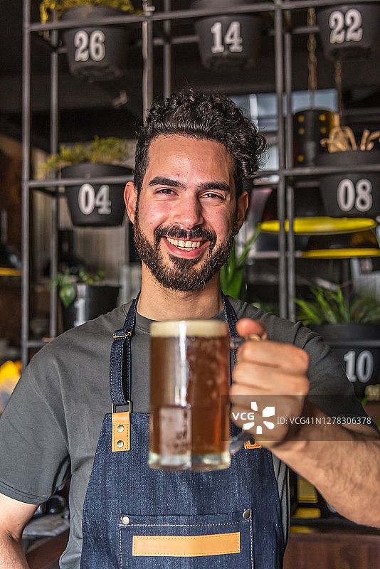 一个微笑着展示啤酒杯的酒保的肖像图片素材