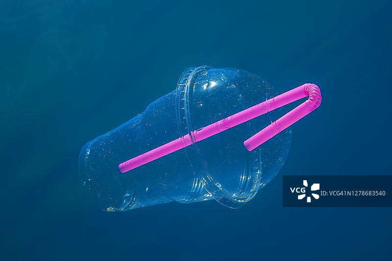 在黑山布德瓦的蓝色水中，一个带吸管的塑料鸡尾酒杯慢慢地漂浮在水下图片素材