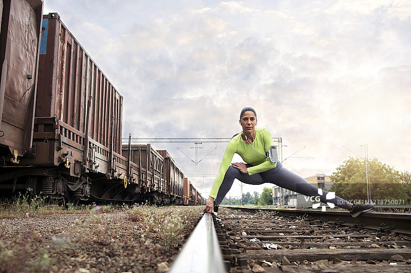 女运动员在铁轨上伸展，准备她的腿进行跑步训练。运动和跑步。在后台的火车和马车上。图片素材