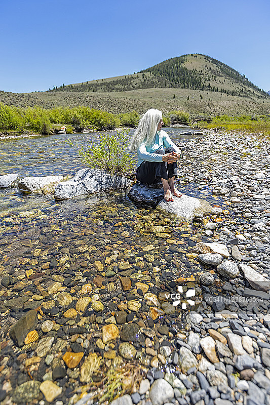 美国，爱达荷州，太阳谷，女人坐在岩石上的河流图片素材
