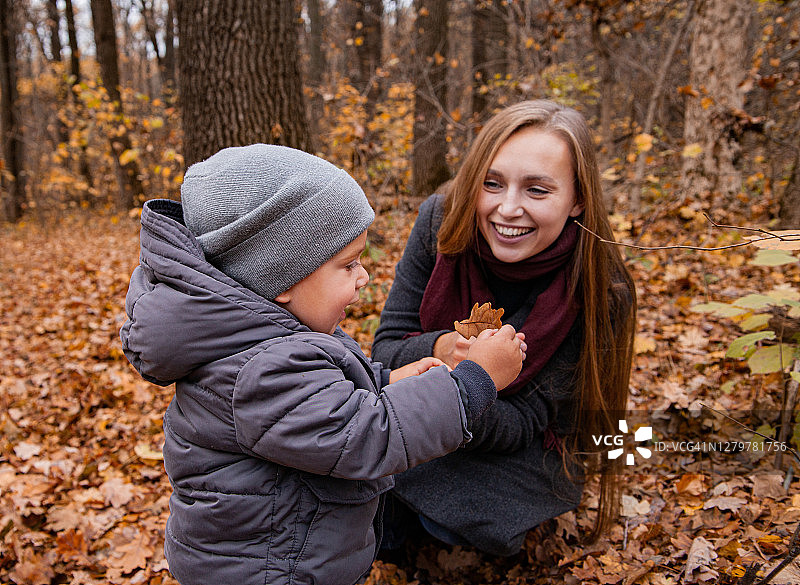 快乐的妈妈和孩子在秋天的森林里玩耍图片素材