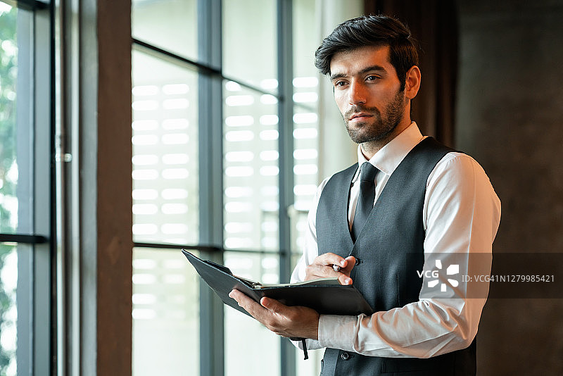 一个帅气的成功商人穿着公司服装在办公室里用笔记本写字。图片素材