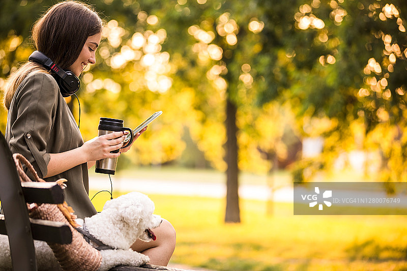 微笑的年轻女子在公园长椅上放松时与朋友发短信图片素材