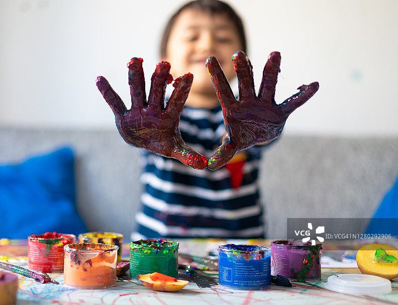 一个富有创造力的学前班小男孩在他的房间里展示他手上的彩色手指彩绘。图片素材