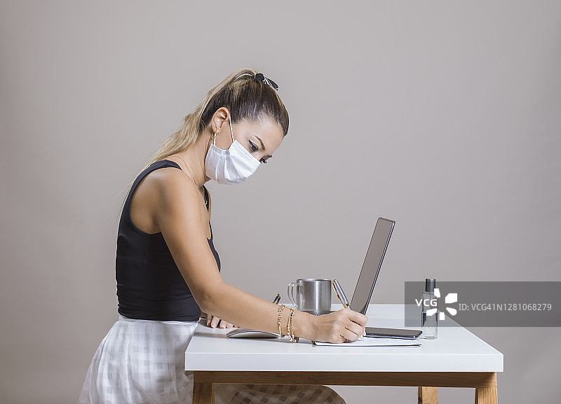 戴着口罩在办公室用笔记本电脑工作的女商人图片素材
