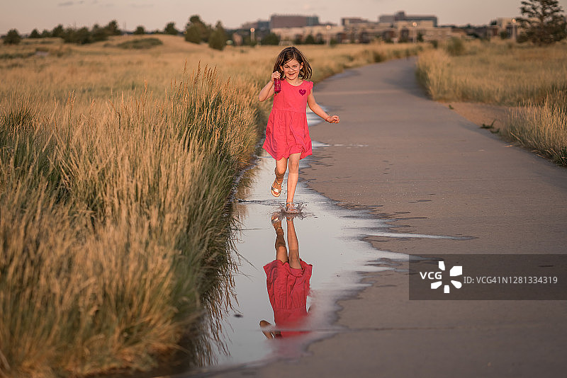 小女孩抱着泡泡跑过附近公园的水坑图片素材