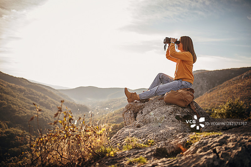 一个女人拿着望远镜坐在日落的山顶上图片素材