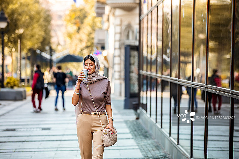 穆斯林成熟女人喝着咖啡走在城市里图片素材