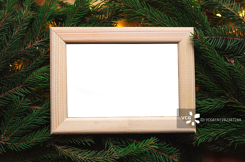 空白的白色木制画框与复制空间。圣诞节天然松树或冷杉树枝为背景。圣诞彩灯，松果和植物天然装饰。图片素材