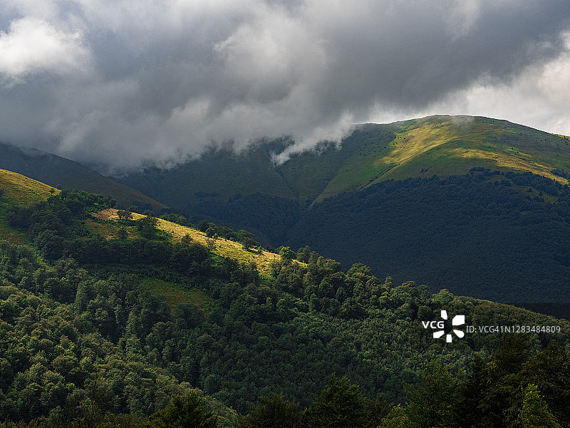 夏季山脉景观与绿色的森林，多云的天空和阳光图片素材