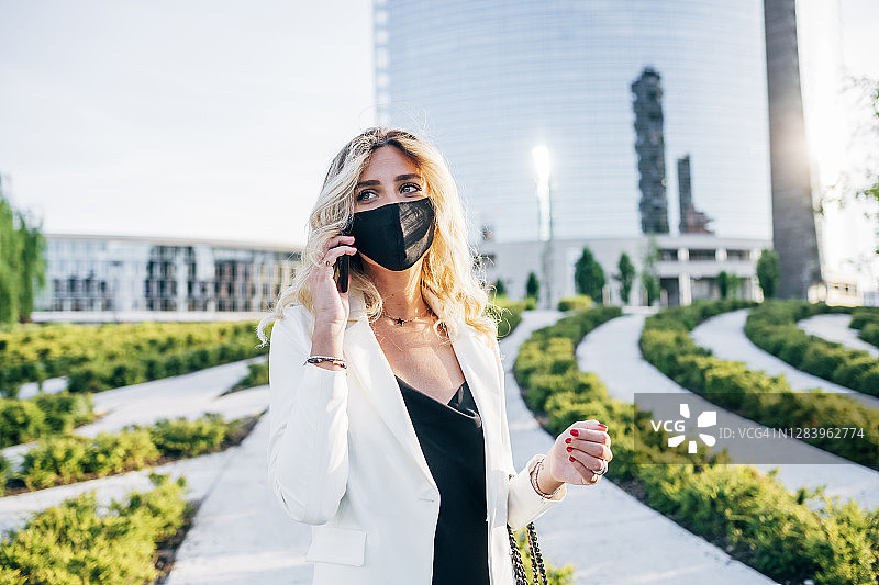女企业家戴着口罩，站在城市里用智能手机聊天图片素材